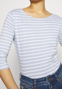 Ljusblå och vit randig långärmad topp med en vid halsringning och en mjuk textur, kombinerad med jeans i klassisk modell.