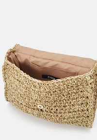 Borsa in paglia naturale intrecciata con fodera in tessuto beige, chiusura a pattina e una tasca interna singola. Presenta un design minimalista.