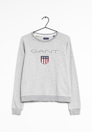 Grauer Sweatshirt mit langen Ärmeln mit dem Schriftzug „GANT“ und einem Wappenlogo mit drei weißen Sternen über roten und weißen Streifen, hängend an einem schwarzen Kleiderbügel.