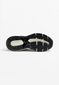 Semelle de sneaker avec une base en caoutchouc noir, des motifs de traction, des accents gris clair et une zone centrale lisse pour une bonne prise.