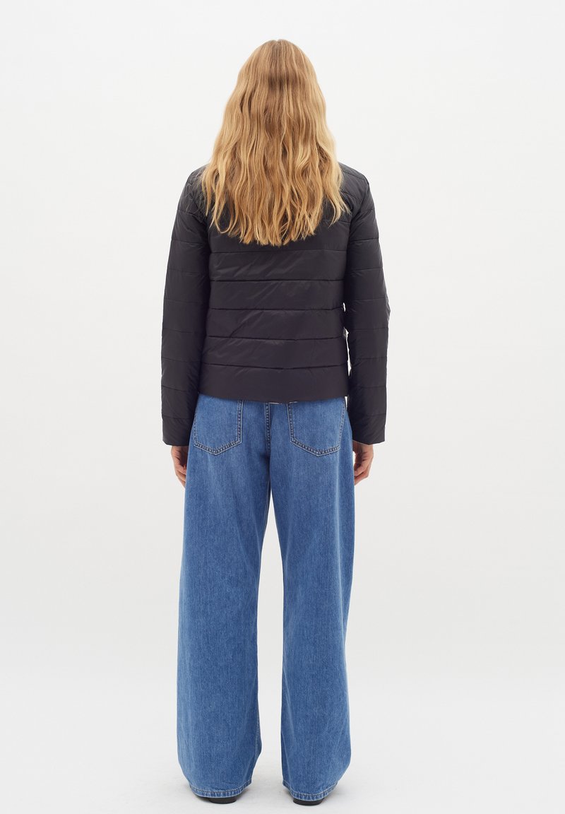 Schwarze gep padded Jacke mit horizontalen Nähten, kombiniert mit lockeren, hellblauen Jeans mit geraden Beinen und Gesäßtaschen.