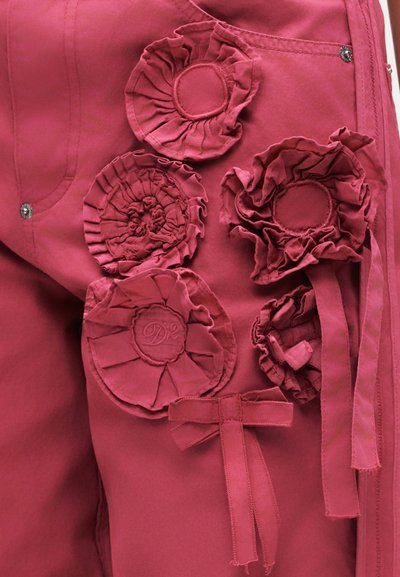 Σκούρο ροζ ύφασμα με πέντε στρογγυλά ξέφτια υφάσματος σε σχήμα λουλουδιών και ένα μικρό φιόγκο ραμμένο στην επιφάνεια.