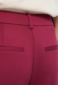 Μαγειντό ρούχο σε ματζέντα από ύφασμα με λεία υφή, που διαθέτει κρυφό ζωνάκι μέσης και δύο οριζόντιες πίσω τσέπες.