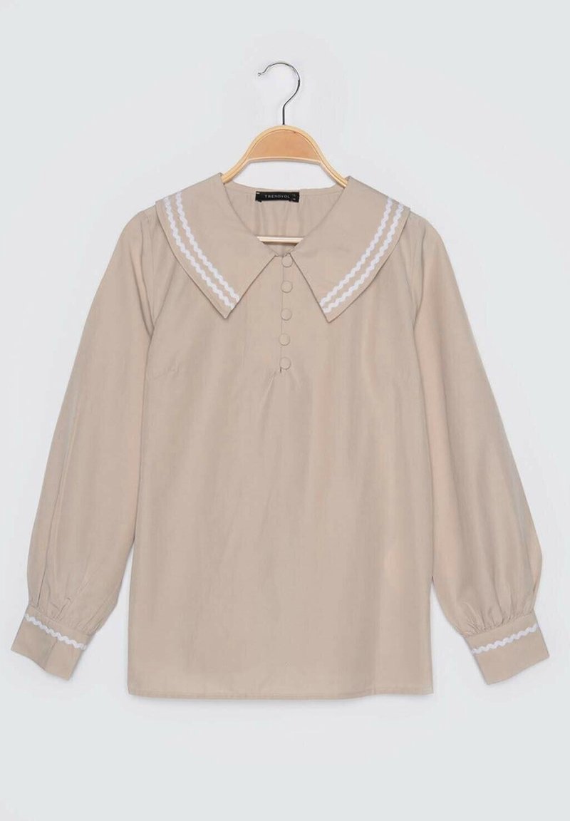 Beige-langärmlige Bluse mit großem weißen Wellenkragen und dekorativen Knöpfen. Puffärmel mit weißem Besatz an den Bündchen.