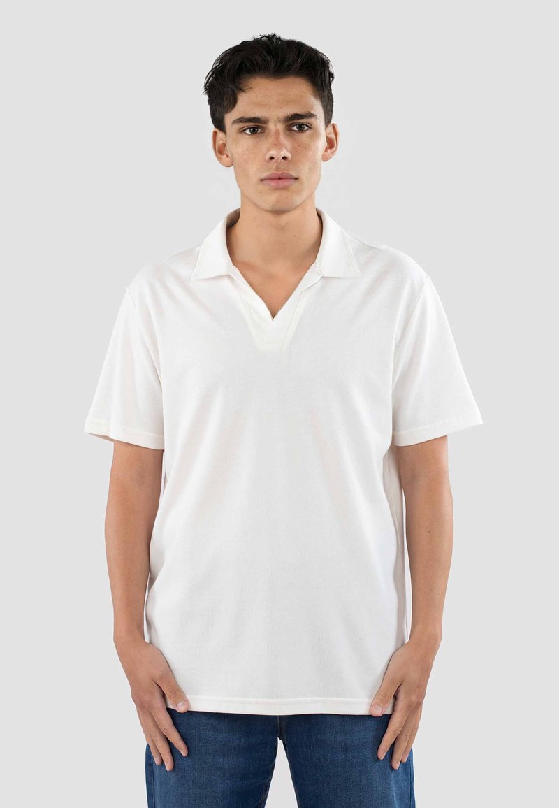 Polo bianco con scollo a V, maniche corte e tessuto testurizzato. Il design è semplice e presenta una vestibilità comoda.