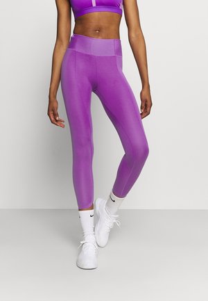 Leggings de sport violets avec une taille haute, texture lisse et coupe ajustée, associés à des baskets blanches et des chaussettes.
