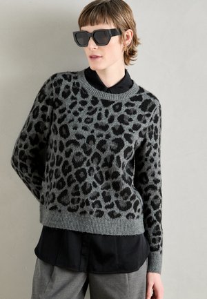 Gray sweater with a black leopard print, round neckline, ribbed cuffs, layered over a black collared shirt, paired with oversized black sunglasses.