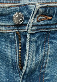 Close-up van denim jeans met een metalen knop, gouden rits en oranje stiksel. Lichtblauwe stof met een licht vervaagd textuur.
