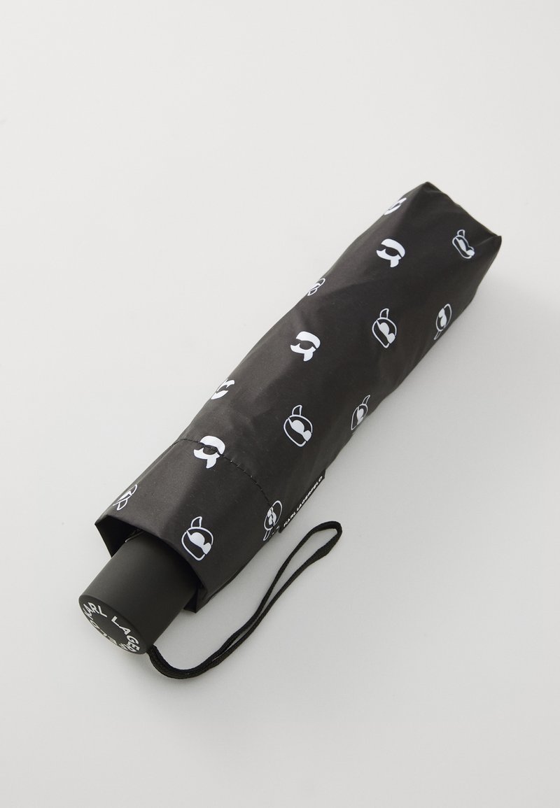 Svart rullparaply med ett tygöverdrag som har vita grafik av olika silhuetter. Inkluderar ett svart handtag med ett handledsband.