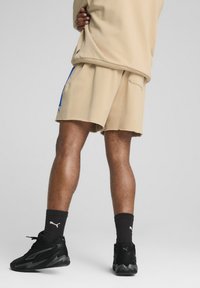 Beige træningsshorts med frynset kant, båret med sorte sneakers og matchende sokker. Stoffet ser blødt ud, med en afslappet pasform og sidelommer.