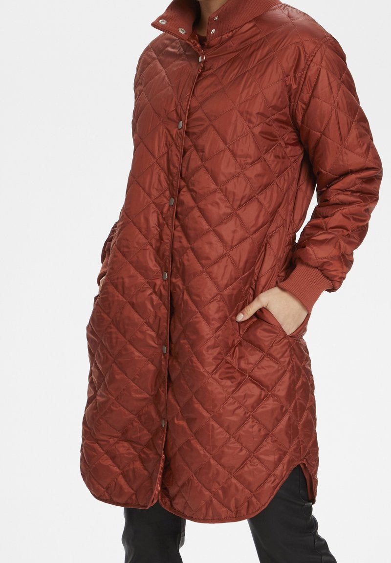 Pikowana długa kurtka w ciemnoczerwonym kolorze, z wysokim kołnierzem, zapięciem na napy i bocznymi kieszeniami. Wykonana z błyszczącego, ocieplanego materiału.