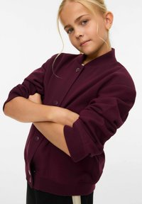 Giacca bomber bordeaux con colletto e polsini a coste, chiusura con bottoni a pressione e tessuto morbido, con una vestibilità rilassata e tasche laterali.