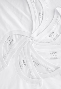Six T-shirts blancs de taille moyenne et coupe régulière, disposés en cercle, montrant les encolures et les étiquettes de la marque.