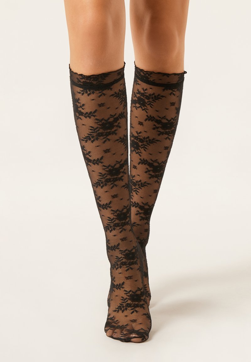 Schwarze kniehohe Strümpfe aus transparentem Stoff mit floralem Spitzenmuster, mit gewellten Rändern und offenem Zehenbereich.
