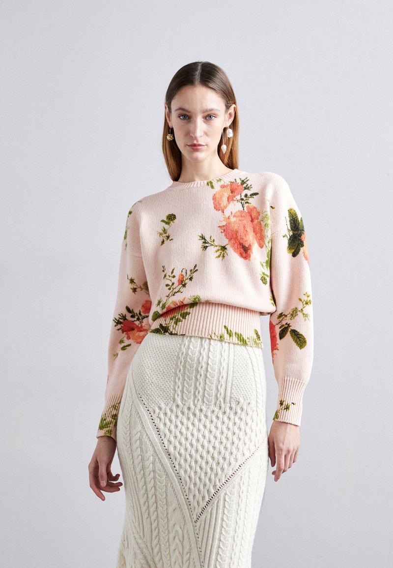 Floral knit sweater in soft pink with green and orange flowers; paired with a textured white cable-knit skirt featuring angular patterns.