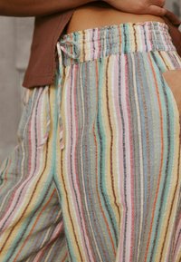 Triibulised laia lõikega püksid, kus vahelduvad värvid: mündiroheline, kollane, roosa ja pruun. Elastne vöökoht ja nööriga detail.