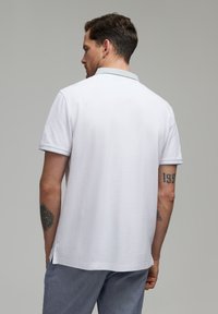 Biała koszulka polo z fakturowanym jasnoniebieskim kołnierzem, krótkimi rękawami, bocznymi rozporkami i gładką bawełnianą tkaniną. Posiada wzór na plecach.