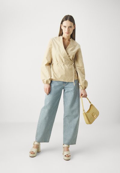 Beige wikkelshirt met lange, elastische mouwen, lichtblauwe wijde jeans, off-white platformhakken en een kleine textuur gele handtas.