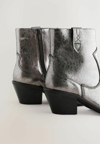 Bottines argentées métalliques avec une finition texturée, dotées d'une fermeture éclair sur le côté, d'un design contourné et d'un petit talon noir. Coutures détaillées.