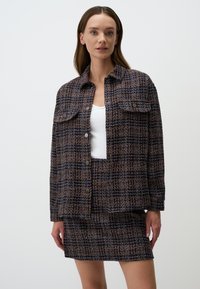 Ensemble jupe et veste en textile tissé avec un motif bleu marine, orange et crème, comprenant deux poches avant et des fermetures à boutons.