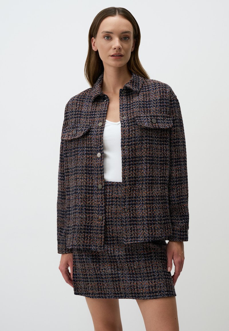 Ensemble jupe et veste en textile tissé avec un motif bleu marine, orange et crème, comprenant deux poches avant et des fermetures à boutons.