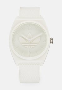 Montre en silicone blanche avec un cadran carré, un bracelet texturé et un logo en relief. Le cadran minimaliste présente des index horaires et des aiguilles simples.