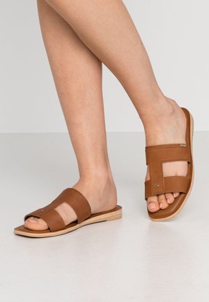 Sandalias planas de cuero marrón con tiras anchas y diseño con recortes. La textura similar a la madera de la suela añade contraste.