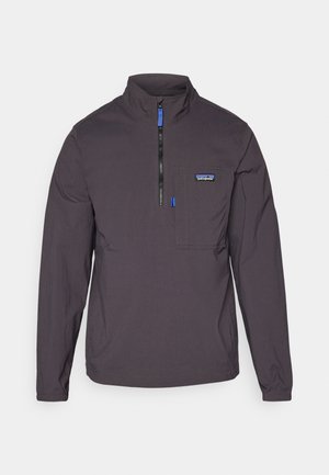 Casaco tipo pullover em tecido cinza escuro com fecho de meia-zíper na frente, colarinho alto e um bolso no peito com detalhe em azul e logótipo.