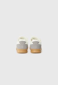 Adidași cu un superior din piele albă și accente din suede gri deschis, având talpa din cauciuc caramel și un design rotunjit.