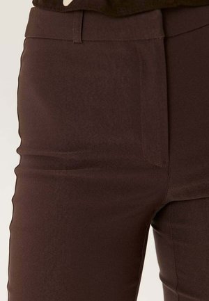 Primo piano di pantaloni marroni aderenti con passanti per cintura e cerniera frontale nascosta.