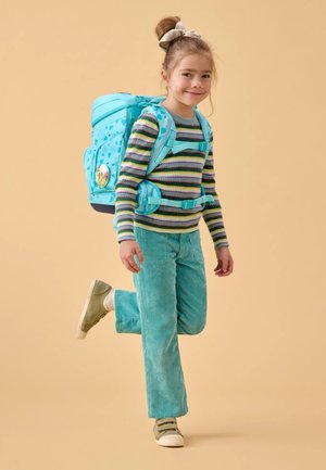 Turquoise backpack with patterned accents, worn by a child in a striped long-sleeve shirt and green corduroy pants, standing against a beige background.