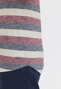 Striped short-sleeve shirt in red, navy, and cream. Features a rounded hem and a small label at the bottom left. Soft, lightweight fabric.