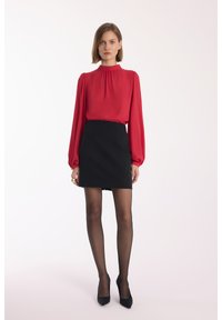 Czerwona bluzka z długim rękawem i wysokim dekoltem, zestawiona z czarną dopasowaną mini spódnicą. Czarne przezroczyste rajstopy i czarne szpilki dopełniają całość.