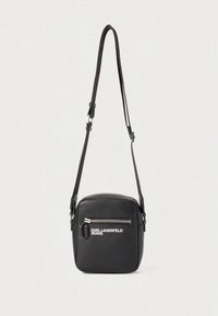 Czarna torba na ramię w kształcie kwadratu z regulowanym paskiem, przednią kieszenią na suwak oraz białym logo "Karl Lagerfeld Jeans" na gładkiej skórze.