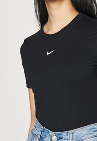 Svart bomullströja med rund halsringning; har en vit Nike-logotyp på bröstet och korta ärmar, i kombination med ljus denim.