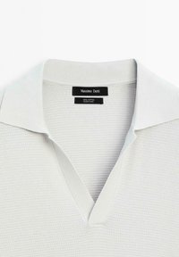 Chemise blanche en coton texturé avec un large col et un col en V de Massimo Dutti, étiquette visible à l'intérieur de l'encolure.