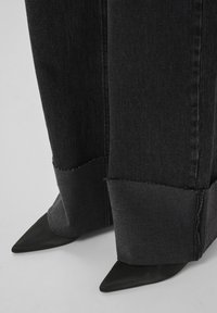 Black denim jeans with a raw hem and wide leg design, paired with pointed black stiletto heels. Focus on texture and bold shapes.