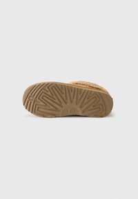 Semelle de chaussure UGG en caoutchouc brun clair, présentant un motif en zigzag, des bords arrondis et un logo embossé. Surface texturée pour une meilleure adhérence.