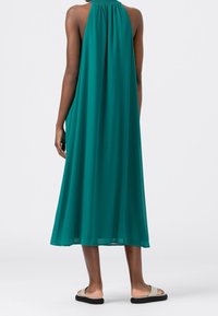 Talfarbenes Maxikleid mit Halterneck aus leichtem Stoff und fließender Silhouette. Bemerkenswertes Rückendesign mit gerafftem Detail am Halsausschnitt.