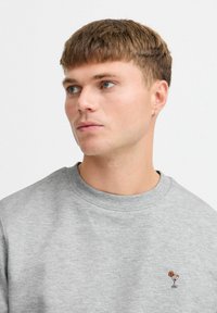 Hallid puuvillasegu sweatshirt halli värviga, millel on ümar kaelus ja väike tikitud kokteiliklaasi disain rinnal.
