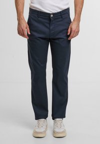 Granatowe bawełniane spodnie o prostym kroju, z zapięciem na guzik, bocznymi kieszeniami i gładką teksturą. Noszone z jasnymi trampkami.