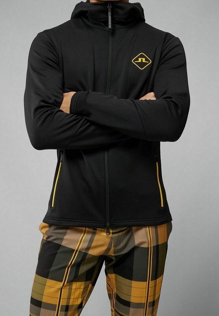 Felpa nera con zip realizzata in tessuto elasticizzato, con un logo giallo sul petto e dettagli gialli sulla zip. Presenta un design aderente e un colletto alto.