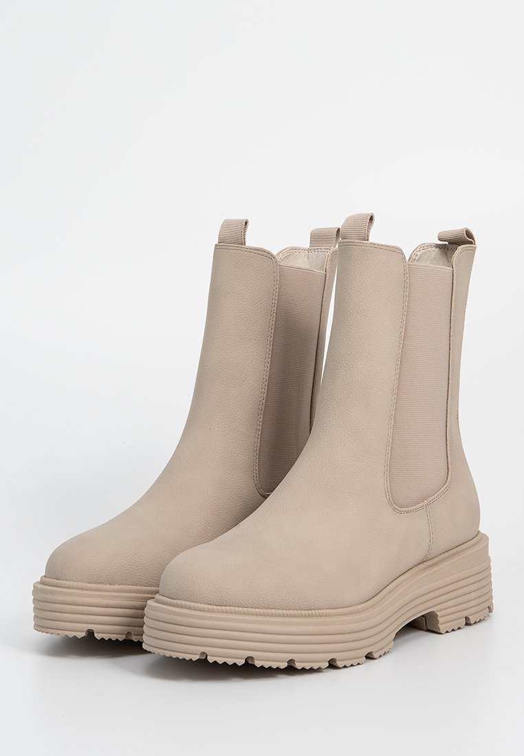 Beige Knöchelstiefel mit einer strukturierten Lederaußenseite, elastischen Seitenteilen und einer dicken, geriffelten Sohle für zusätzlichen Halt und Stabilität.