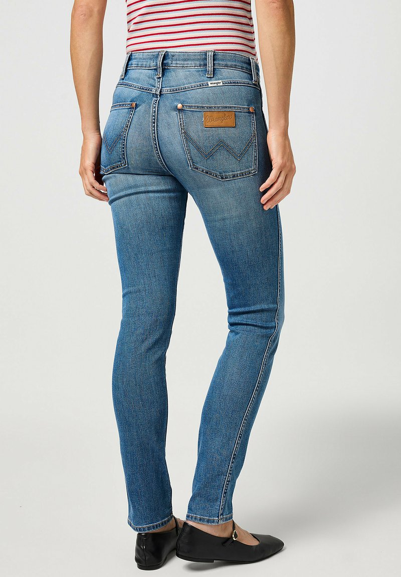 Jeans denim skinny di colore azzurro chiaro con una superficie liscia, vita media e cuciture a contrasto. Presentano un'etichetta in pelle e tasche posteriori.