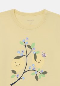 Ljust gult bomulls-t-shirt med en tryckt design av två leende citroner på en gren med gröna blad och blå blommor, samt en snigel.