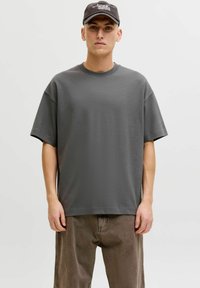 T-shirt gris surdimensionné avec un col rond et des manches courtes, en tissu doux. Associé à un pantalon marron ample.