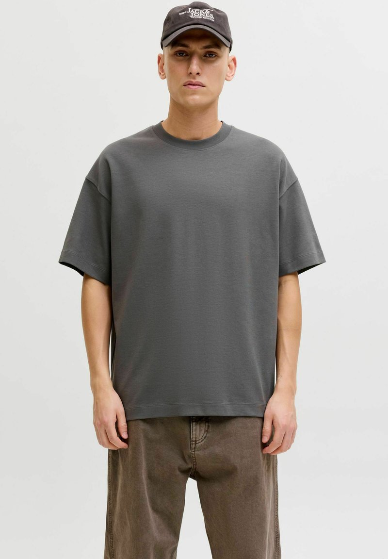 T-shirt gris surdimensionné avec un col rond et des manches courtes, en tissu doux. Associé à un pantalon marron ample.