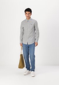 Striped long-sleeve shirt, blue jeans, white sneakers, and olive green tote bag; features button-up front and cuffs, with a slim fit design.