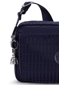 Borsa a tracolla in nylon blu navy con texture trapuntata, tasca frontale, hardware argentato e un ciondolo decorativo a forma di robot attaccato.