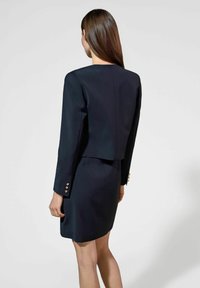 Granatowy zestaw żakietu i spódnicy wykonany z gładkiego materiału, z krojonym fasonem żakietu i złotymi guzikami na rękawach.